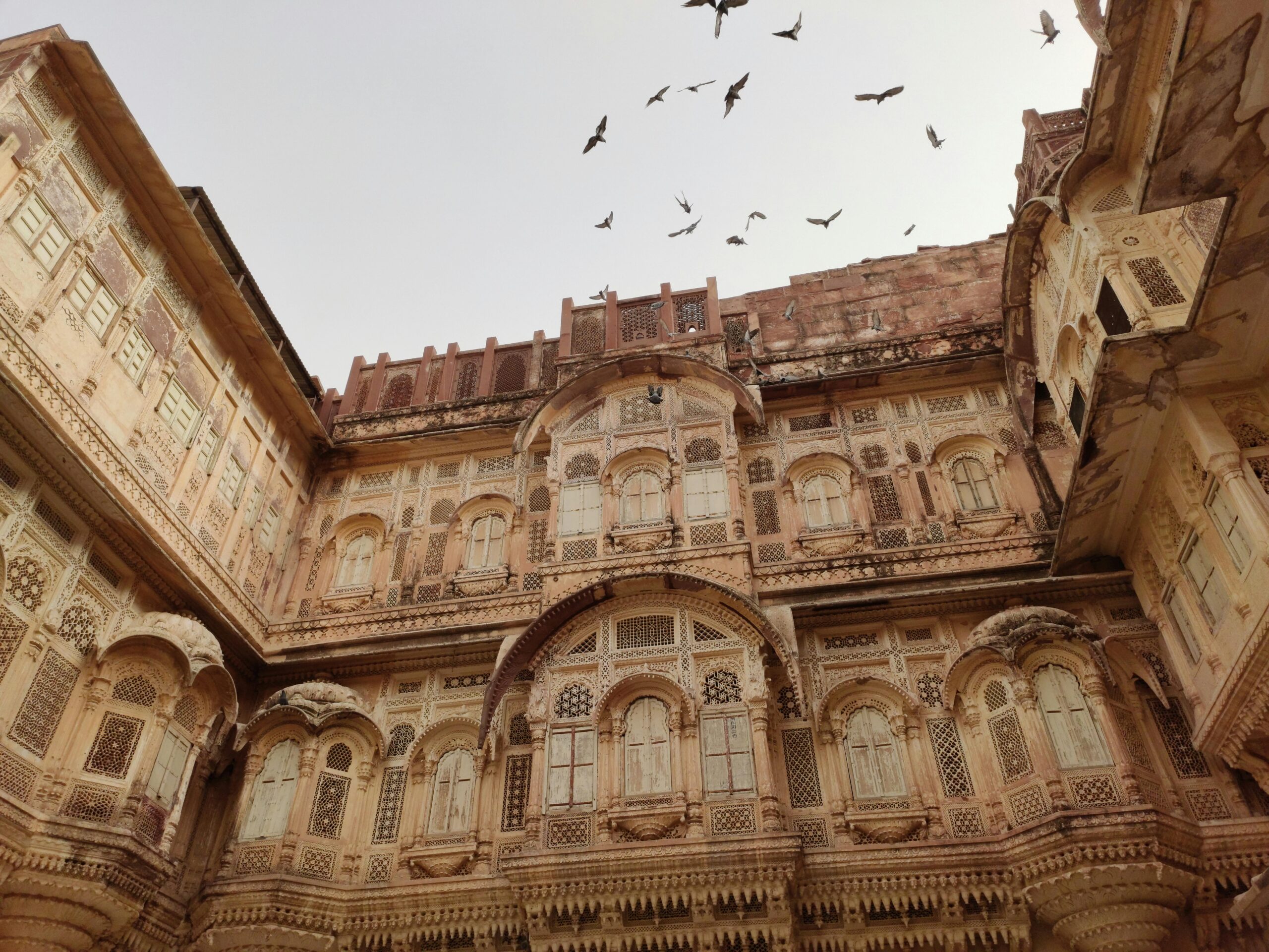 Explore the intricate architecture of Mehrangarh Fort in Jodhpur with birds soaring overhead, captured during the day.